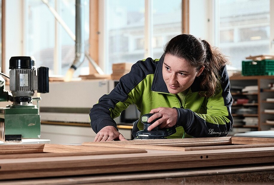 Schreinerin schleift mit der Schleifmaschine ein Stück Holz.