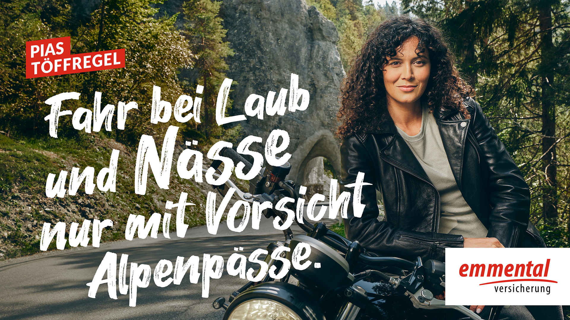 Werbevideo mit dem Slogan "Fahr bei Laub und Nässe nur mit Vorsicht Alpenpässe.", dass eine junge Motorradfahrerin mit schwarzer Lederjacke zeigt, wie sie sich an Ihr Motorrad anlehnt.