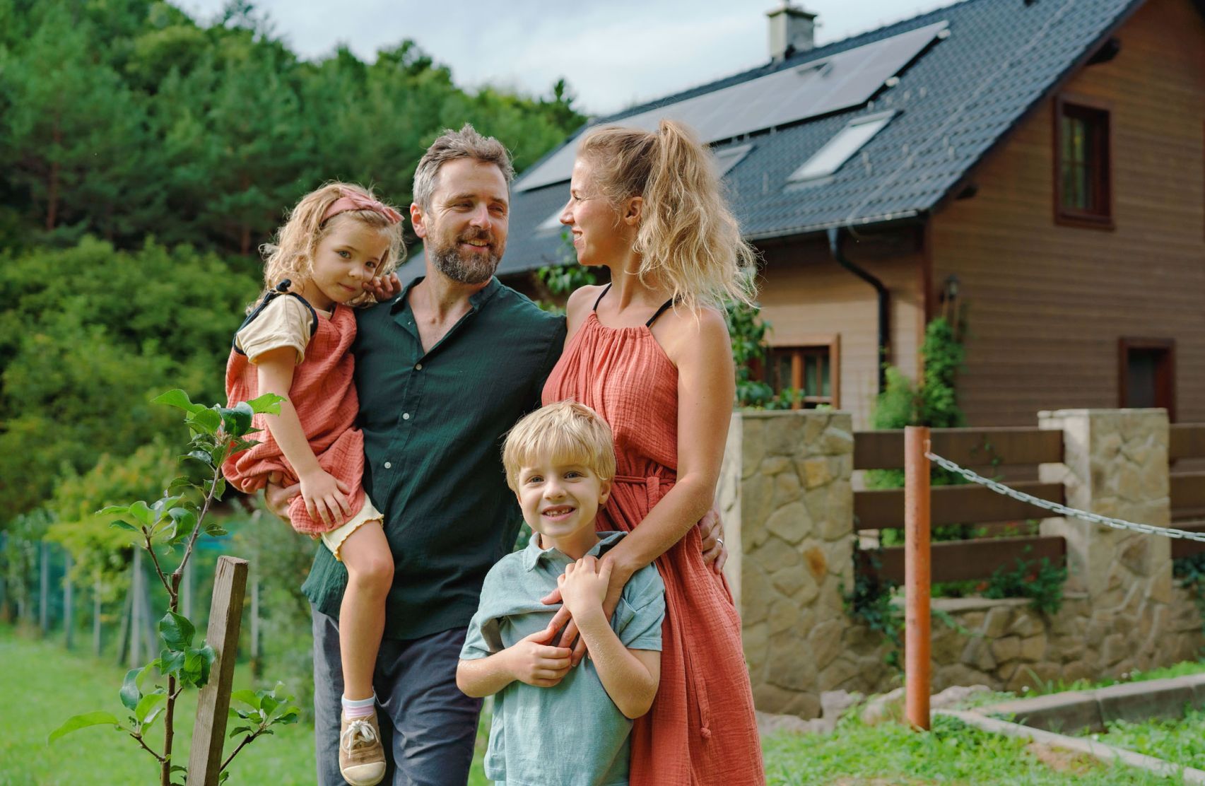 Eine junge Familie mit zwei Kindern steht vor ihrem Haus in einer ländlichen Region.