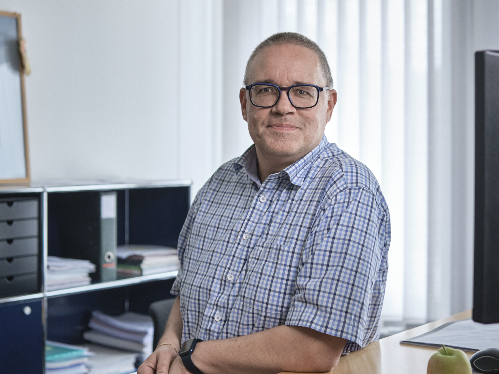 Ein Mitarbeiter der emmental versicherung steht vor seinem Stehpult und schaut freundlich in die Kamera.