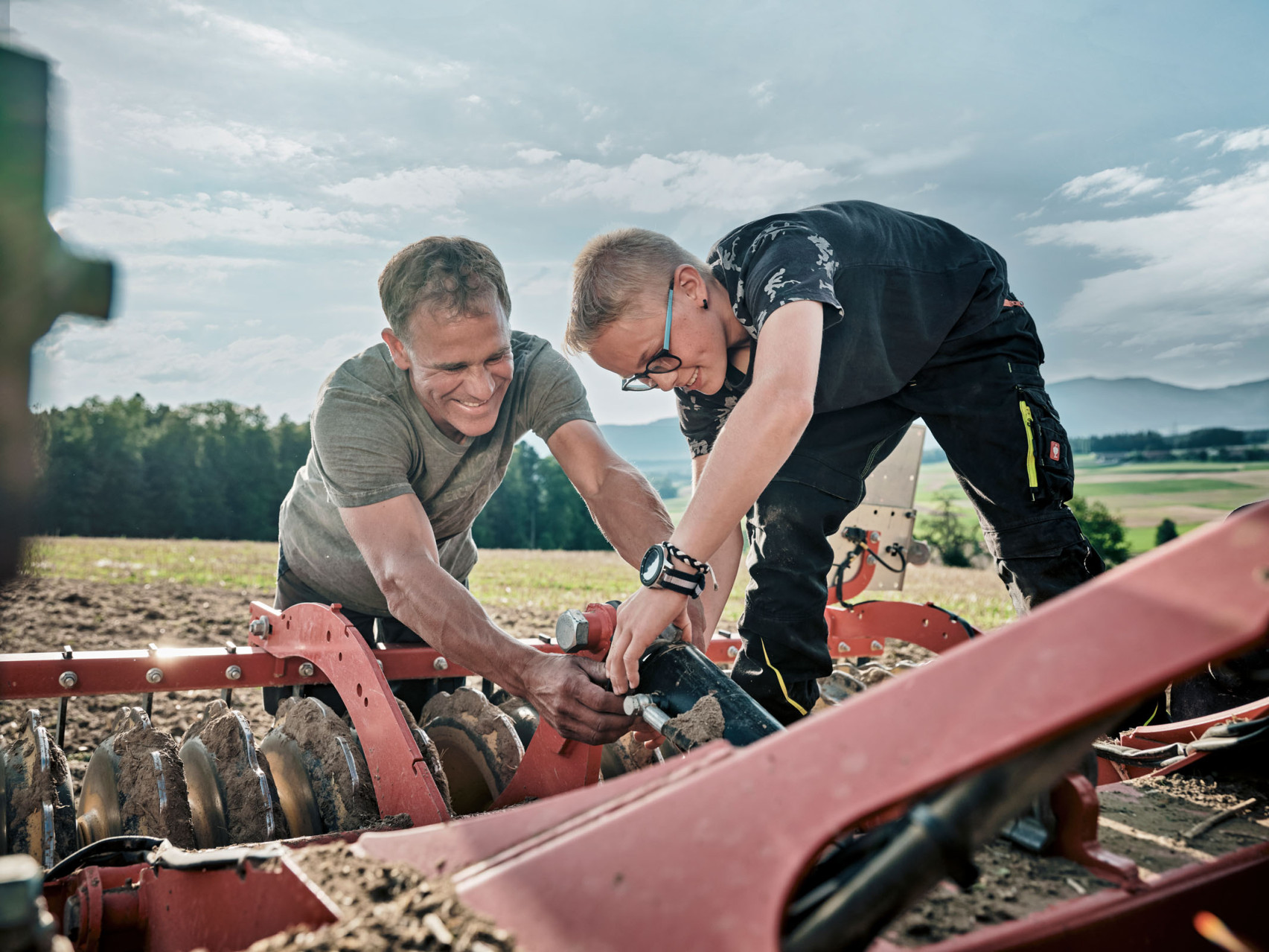 Ein Bauer und sein Sohn schliessen gemeinsam das Acker-Pfluggerät an den Traktor an.