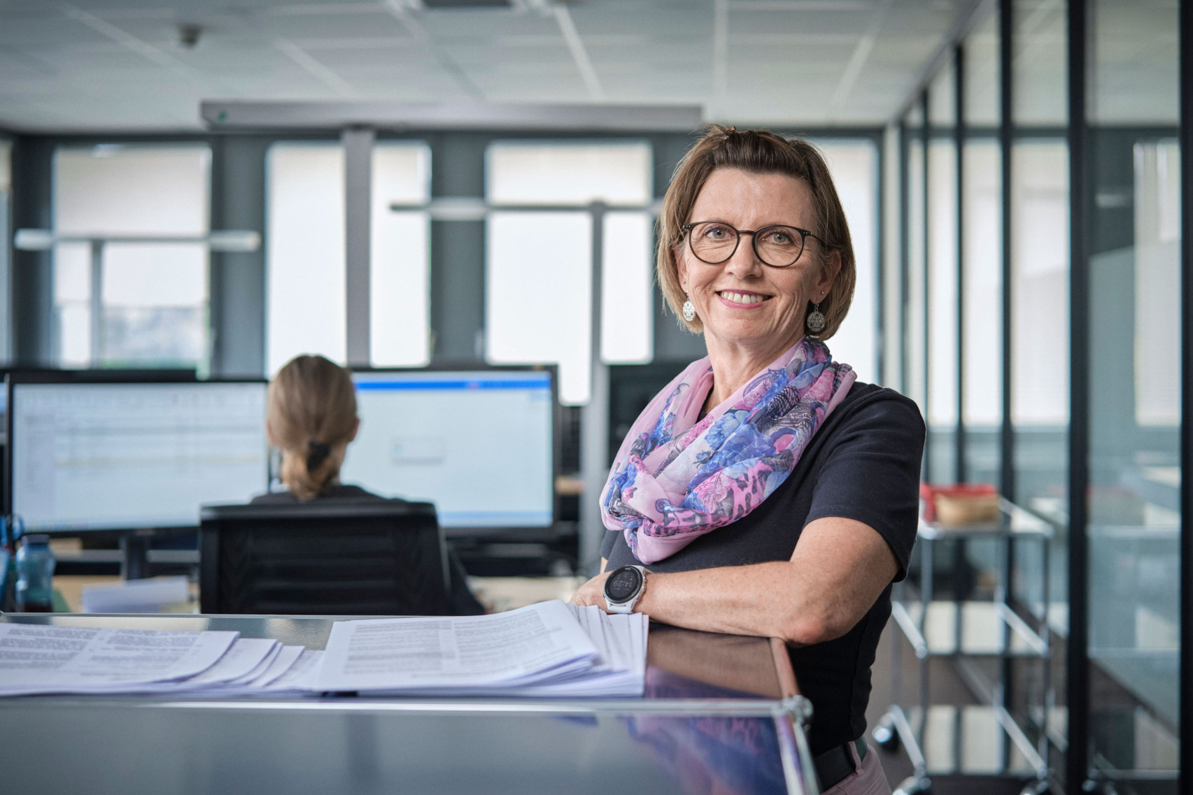 Eine Mitarbeiterin der emmental versicherung steht vor einem hüfthohen Bücherregal und lächelt freundlich in die Kamera.