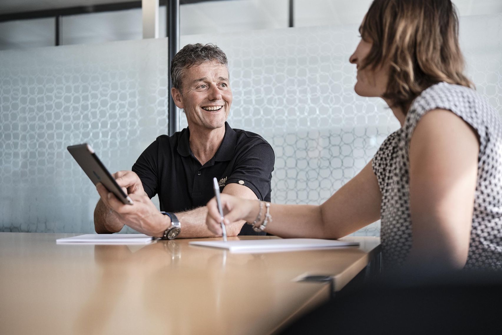 Ein Mitarbeiter der emmental versicherung befindet sich sitzend in einem Beratungsgespräch mit einer Kundin und zeigt ihr etwas auf seinem Tablet.