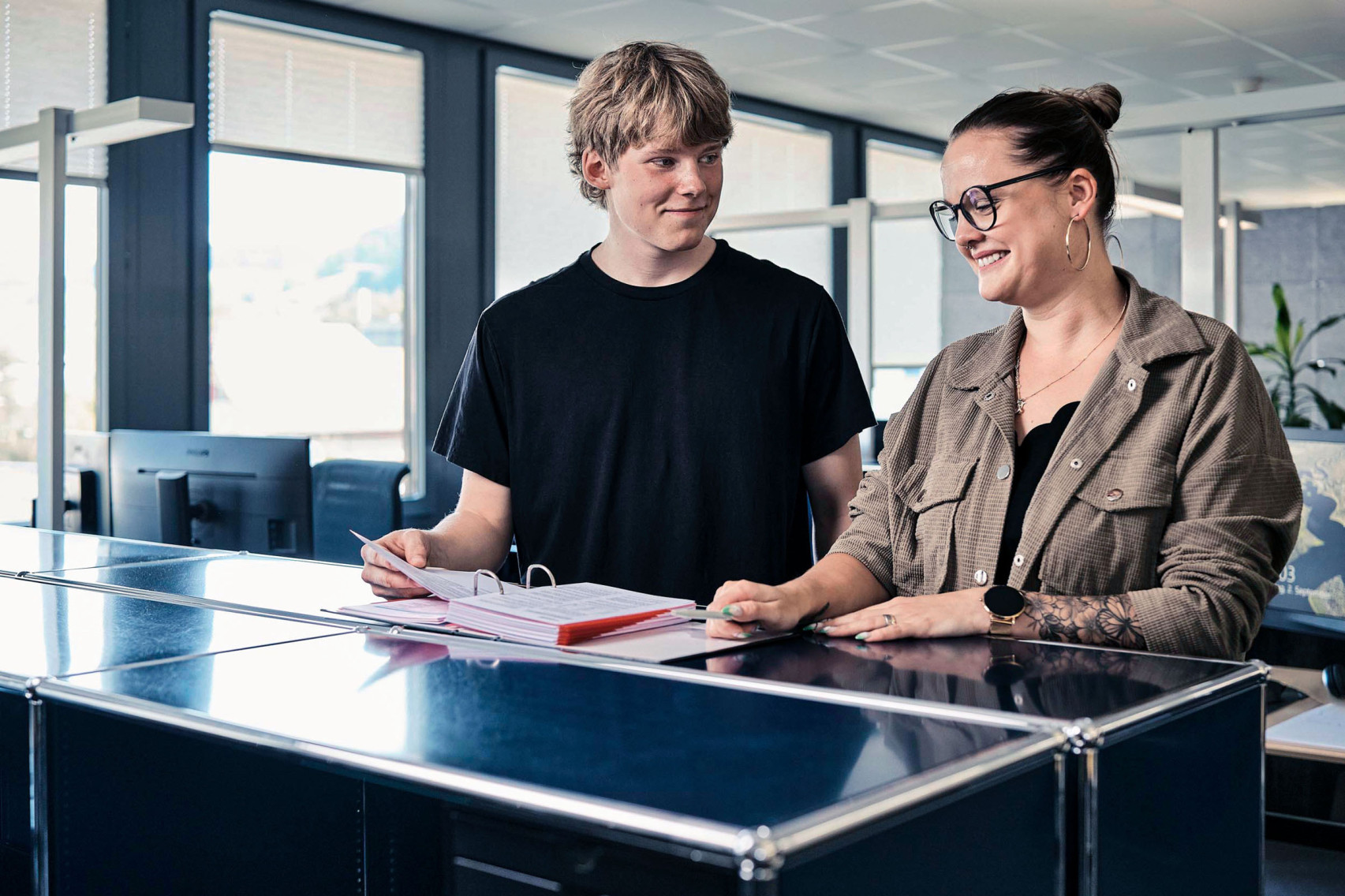 Eine Mitarbeiterin der emmental versicherung zeigt und erklärt einem Lernenden die Verkaufsunterlagen.