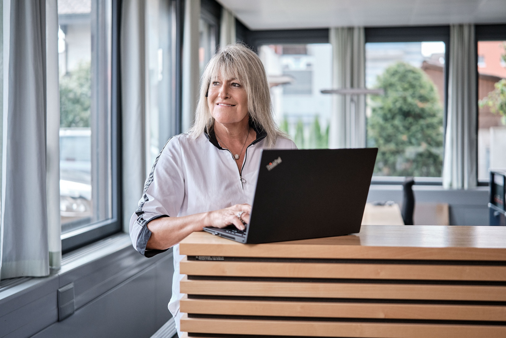Eine Mitarbeiterin der emmental versicherung arbeitet stehend an ihrem Notebook und telefoniert dabei über ihr Headset.