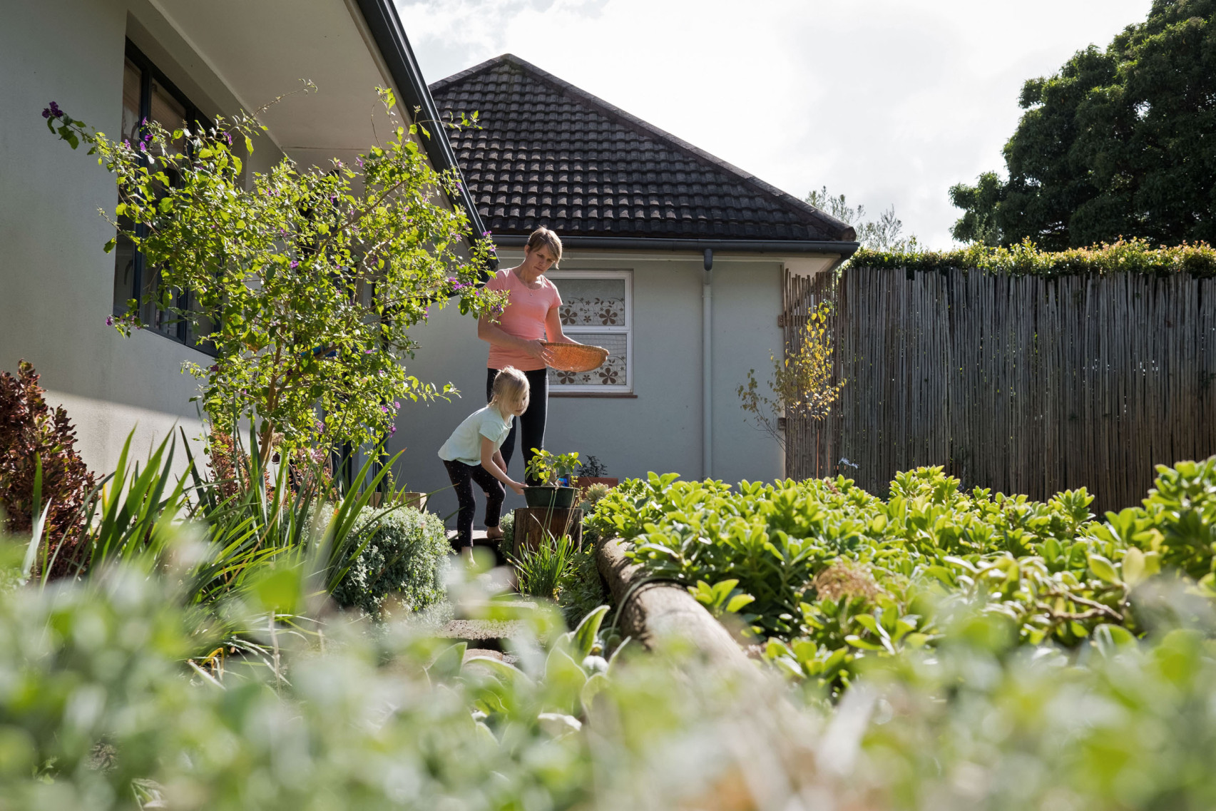 Eine Frau steht mit ihrem Kleinkind im eigenen Gemüsegarten und erntet ihr Gemüse.