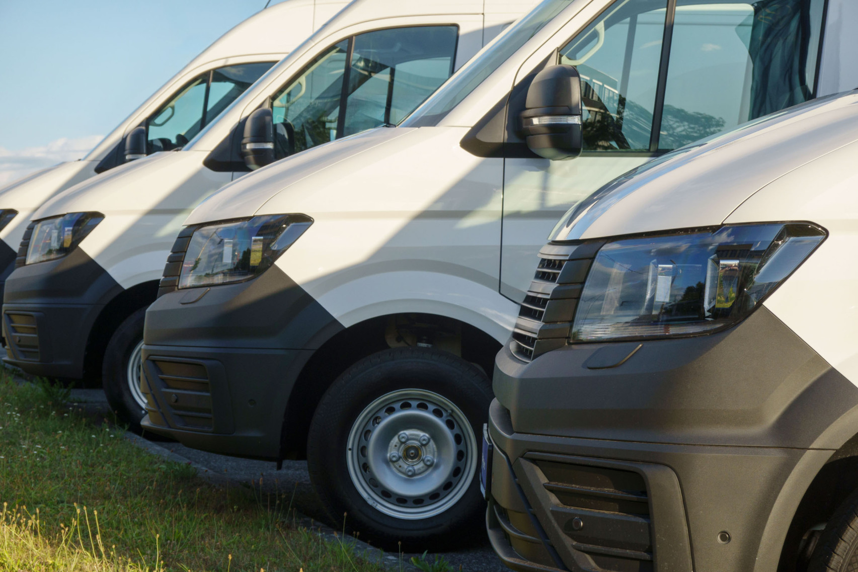 Vier Transport-Wagen eines Unternehmens stehen nebeneinander auf dem Firmenparkplatz.